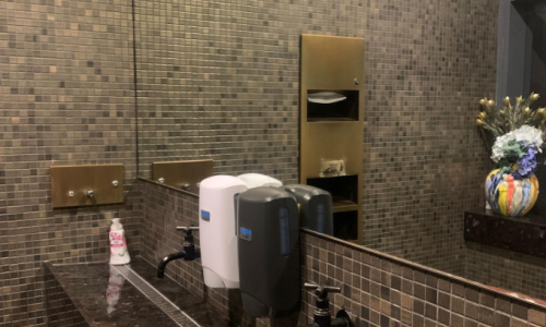 A high-end commercial restroom featuring dark marble vanities, mosaic tile walls, and large mirrors. The surfaces are polished and streak-free, showing reflections of black faucets and soap dispensers, illustrating professional cleaning standards at a Barangaroo venue.